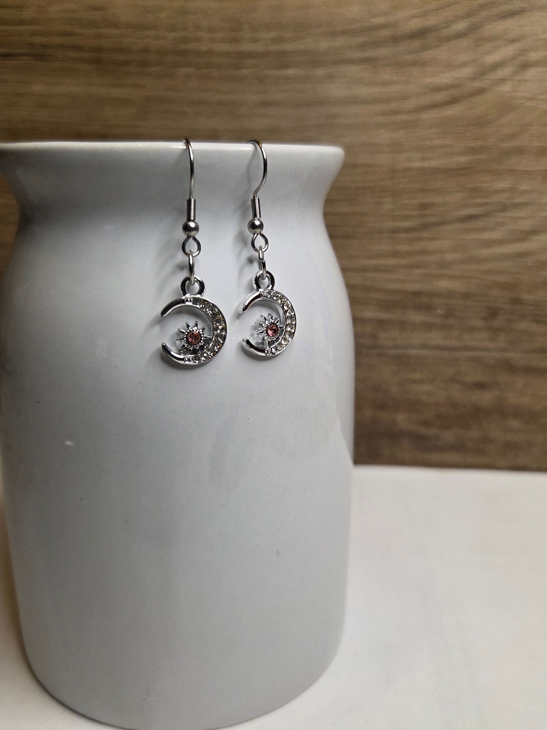 Zilveren, maanvormige oorbellen met een klein roze edelsteentje erin, tentoongesteld in een witte pot.