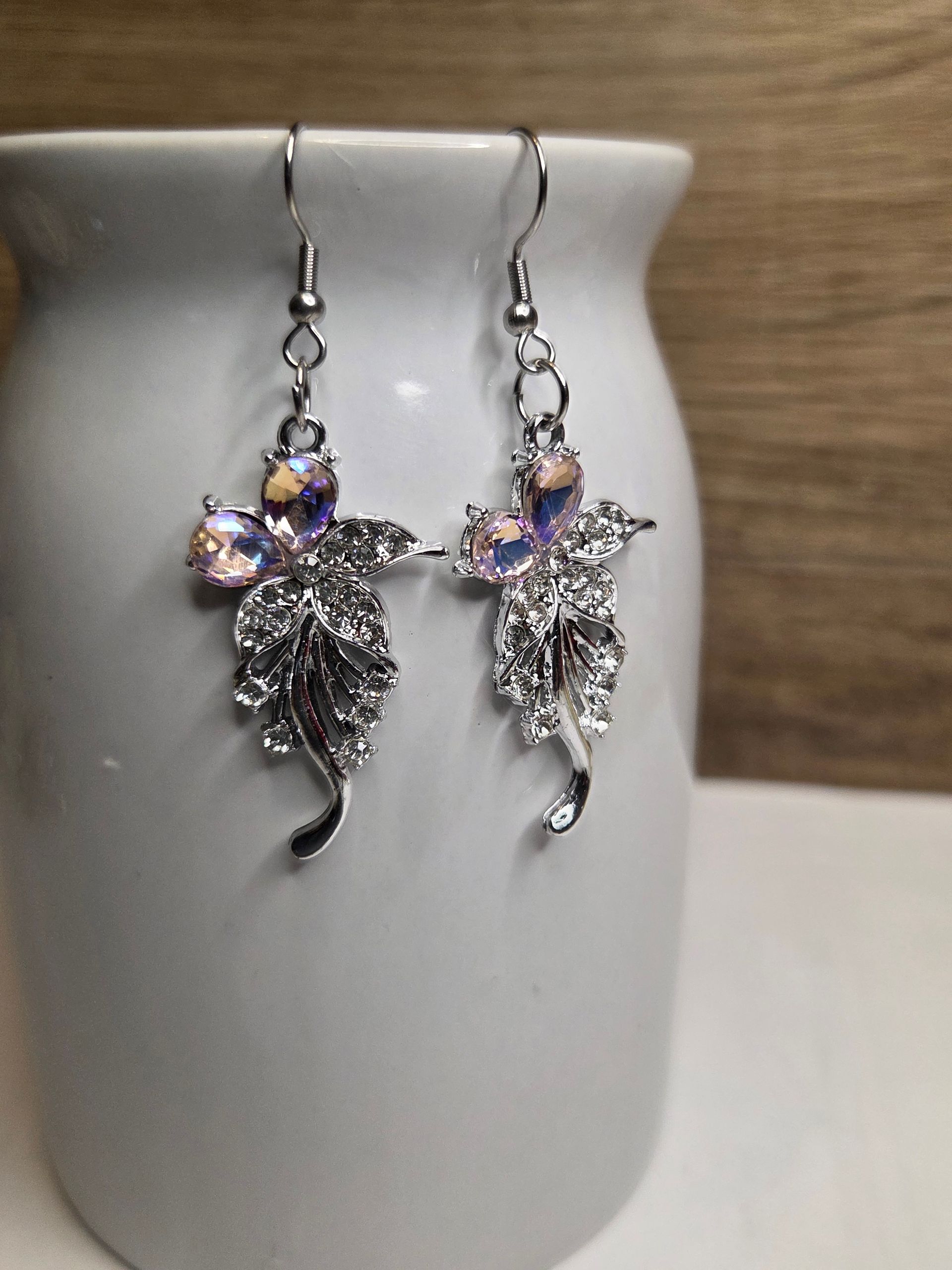 Zilveren oorbellen in de vorm van bladeren met iriserende steentjes, hangend aan een witte vaas.