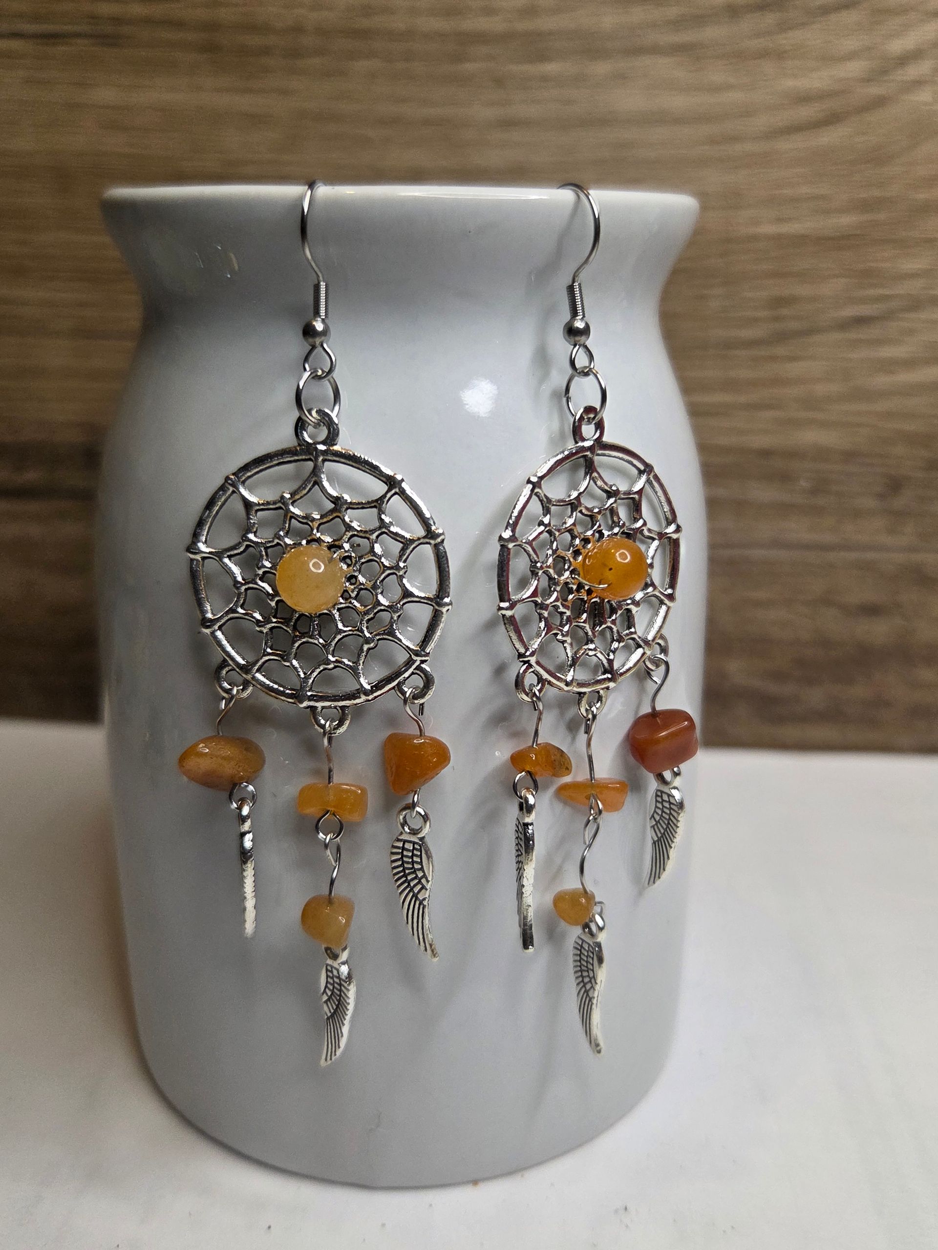 Dromenvanger-oorbellen met amberkleurige kralen en zilveren accenten, gepresenteerd op een witte vaas.