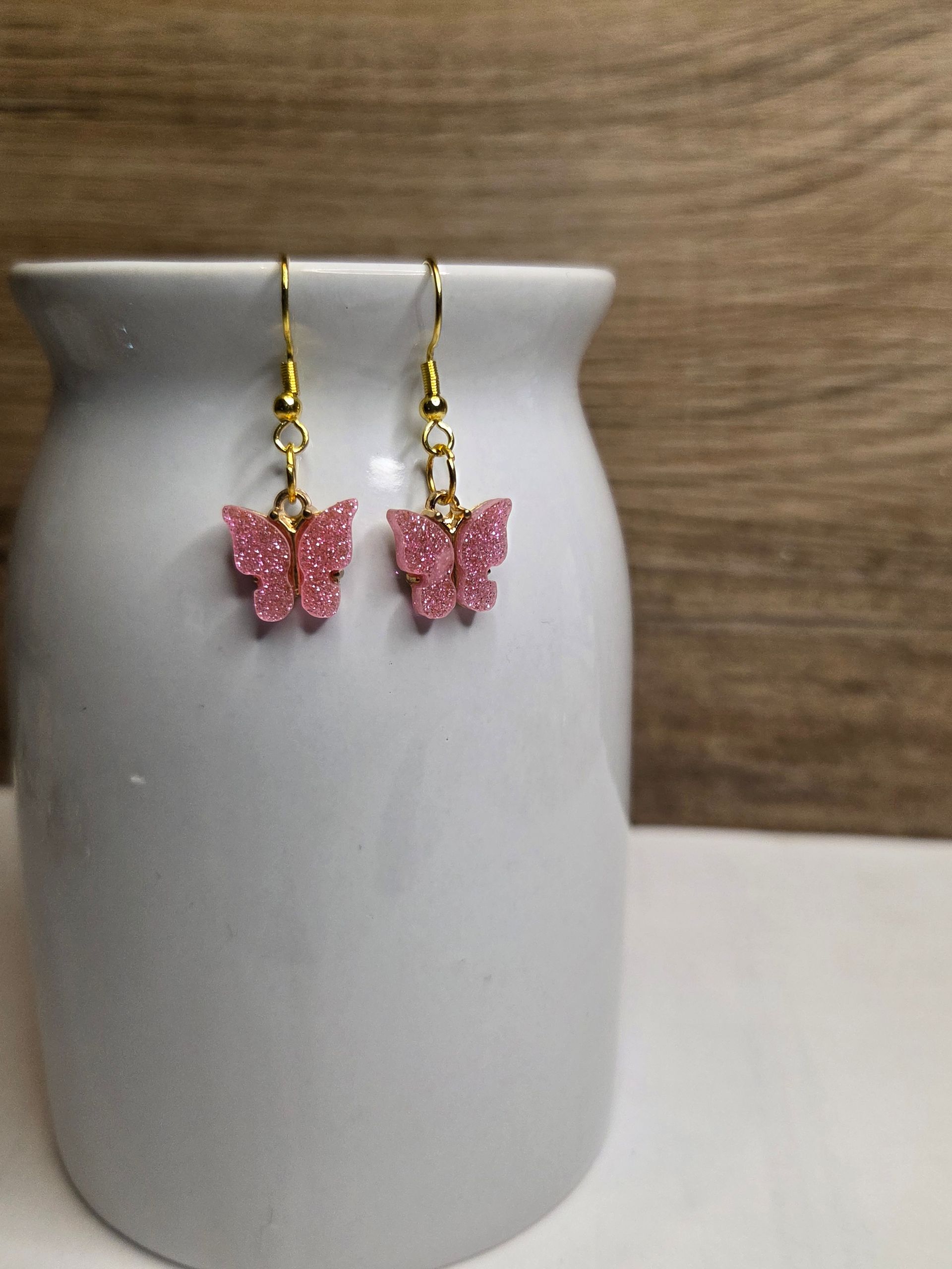 Roze vlinderoorbellen hangen aan gouden haakjes in een witte pot.