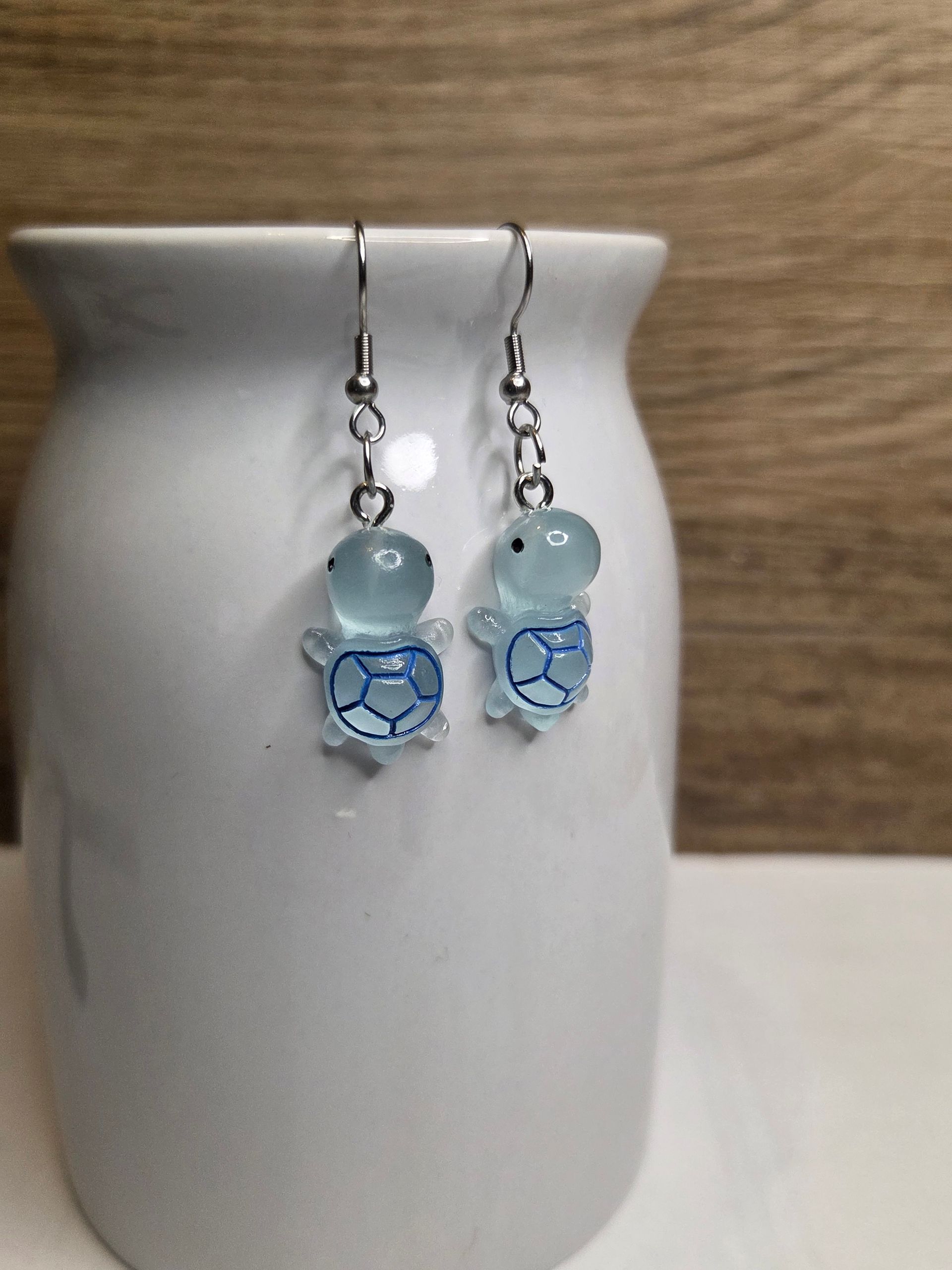 Oorbellen met een blauwe schildpad, hangend aan een witte vaas.