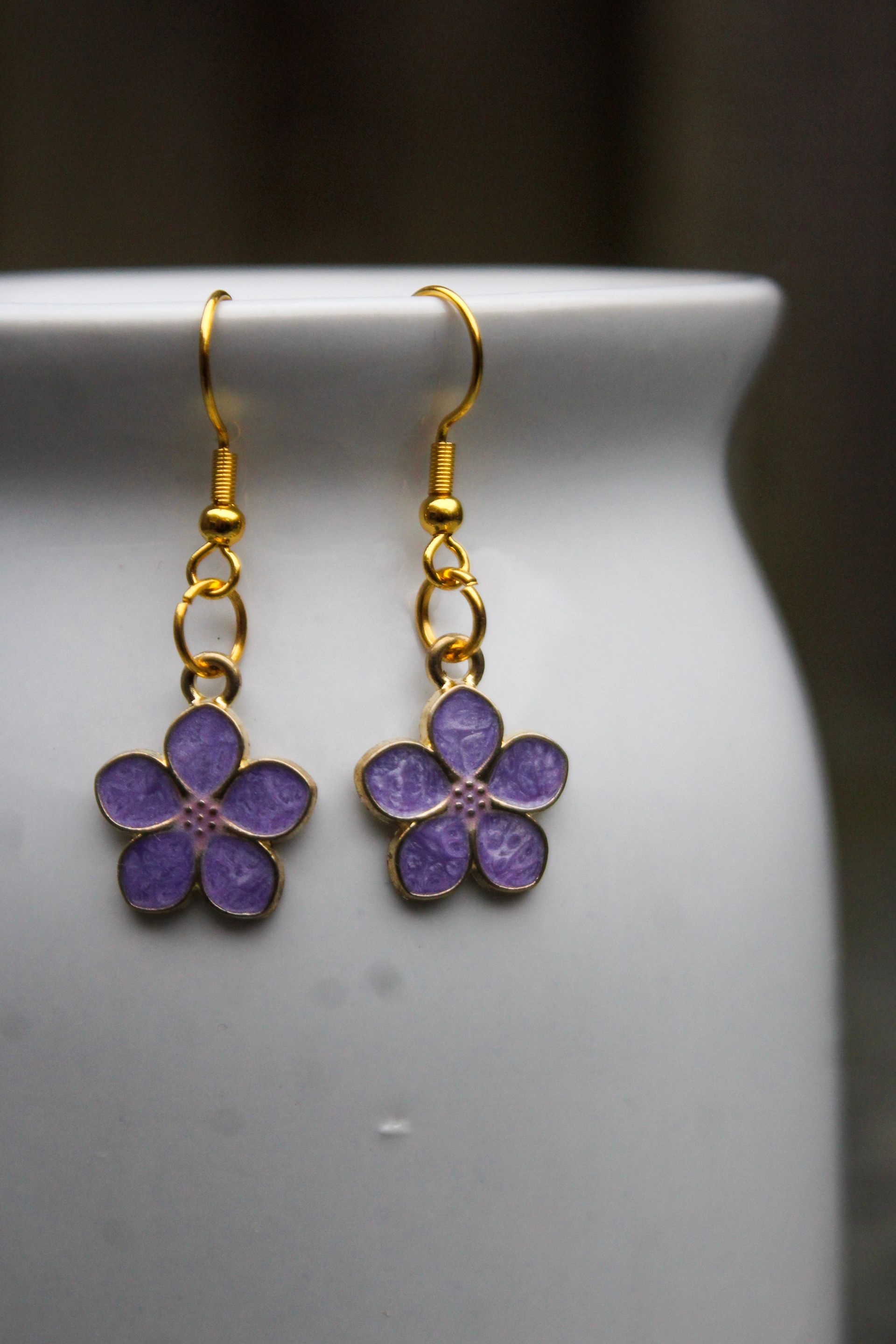 Gouden oorbellen met paarse bloemhangers.
