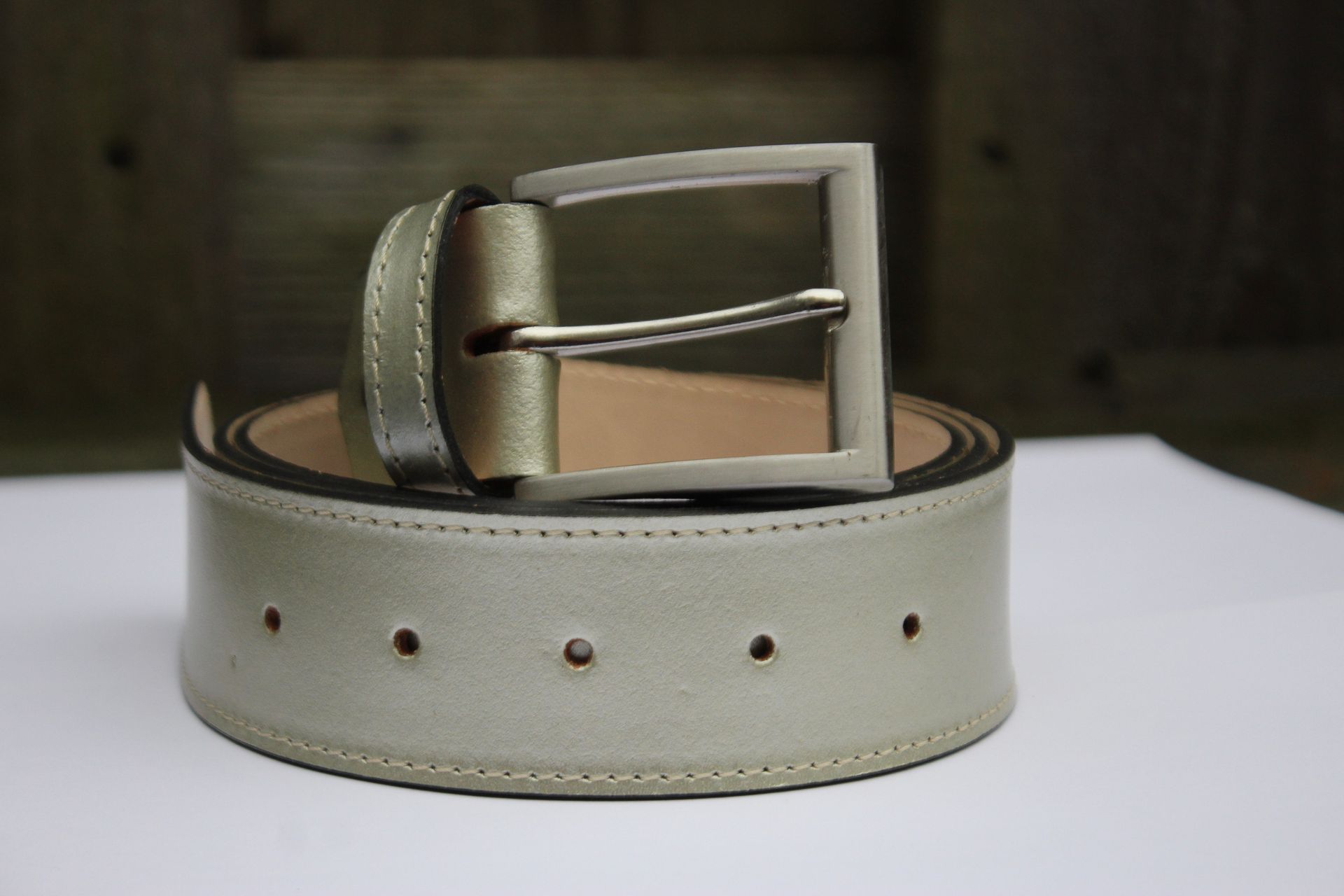 Bruine leren riem met zilveren gesp, opgerold op een witte ondergrond.