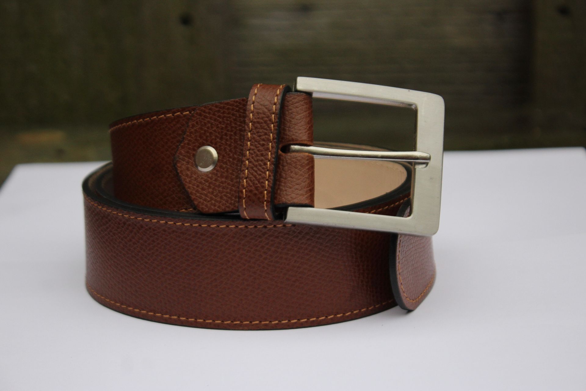 Bruine leren riem met een zilveren gesp, gerold op een witte ondergrond.