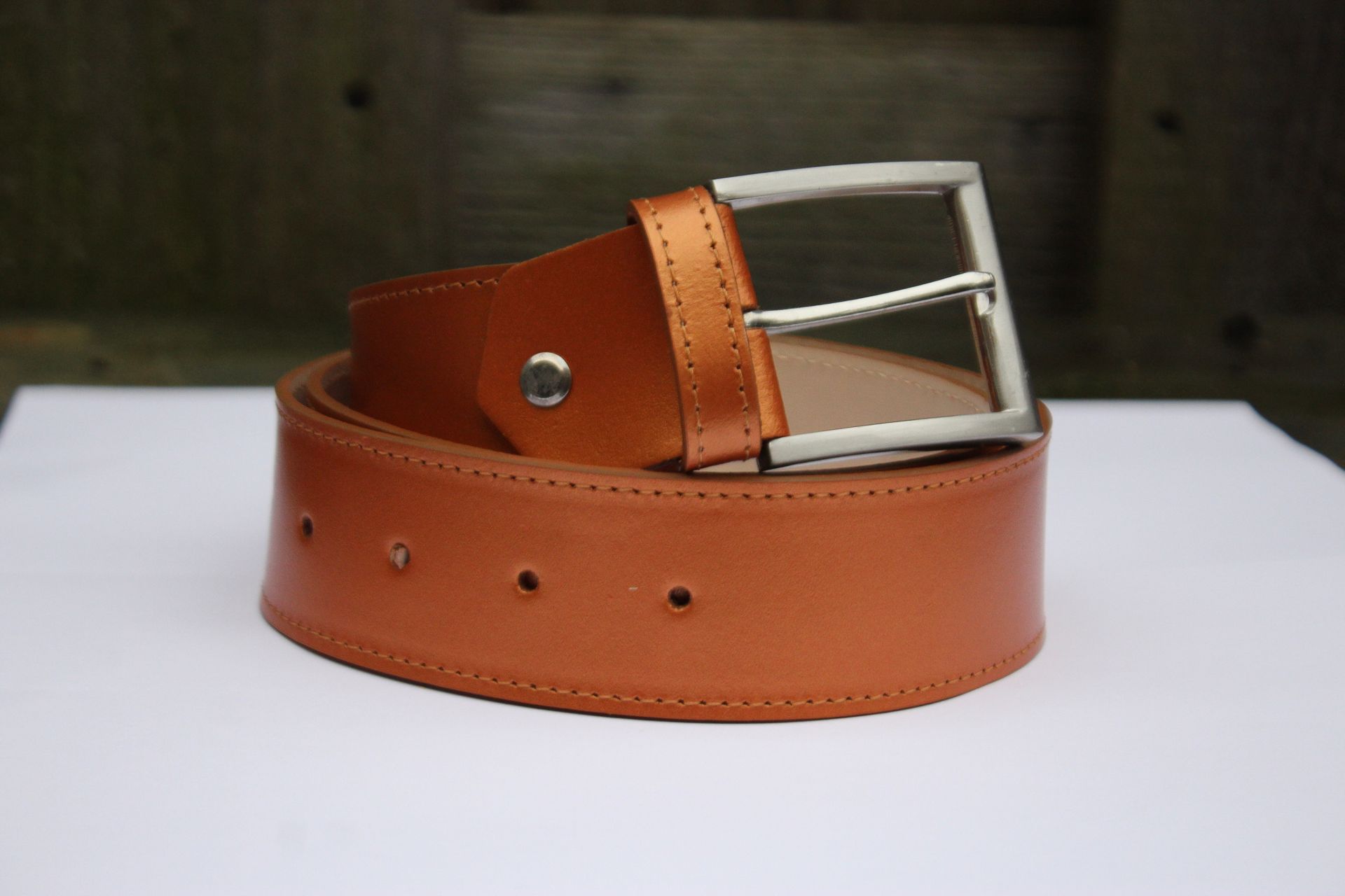 Bruine leren riem met zilveren gesp, rustend op een witte ondergrond.