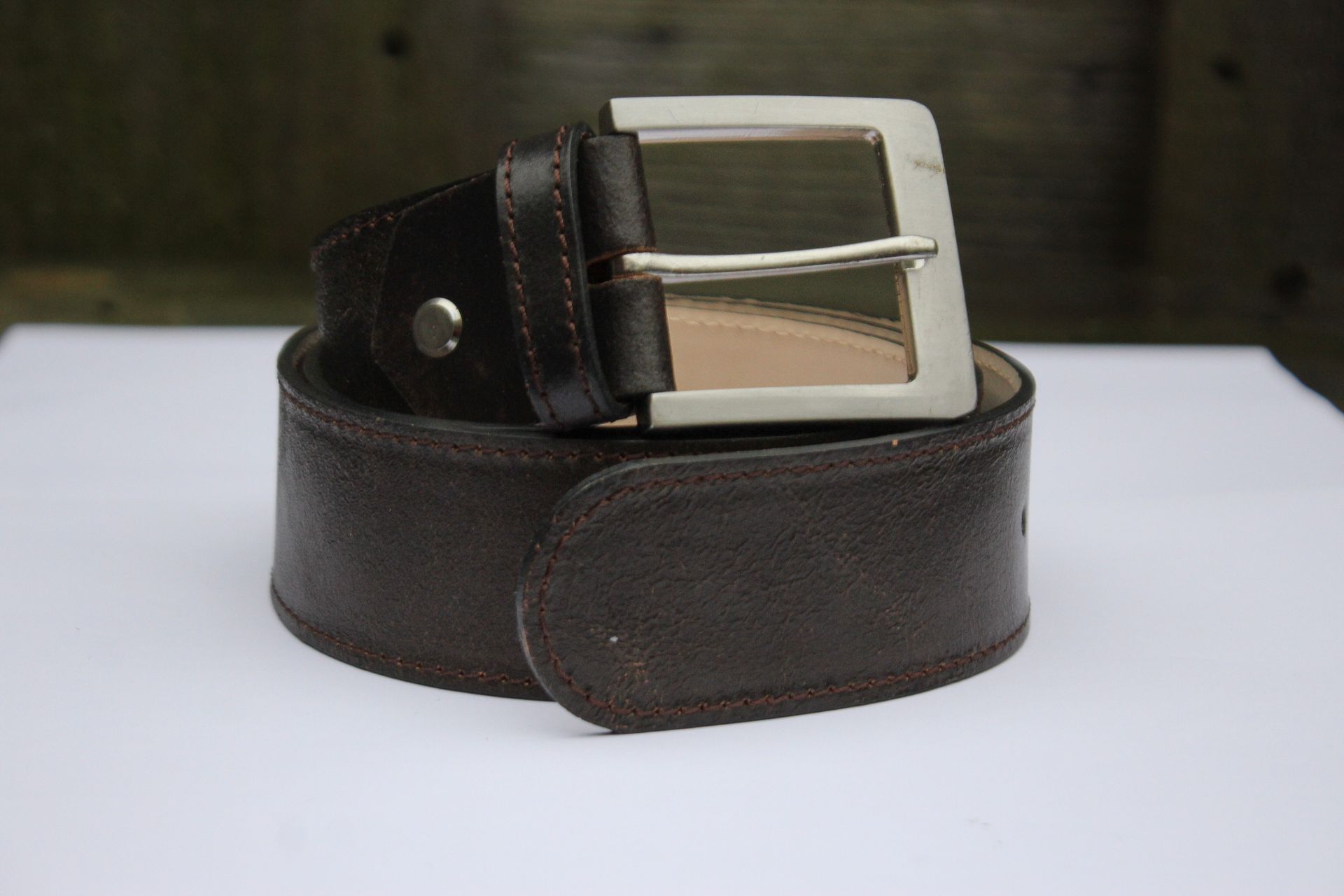 Bruine leren riem met zilveren gesp, liggend op een witte ondergrond.