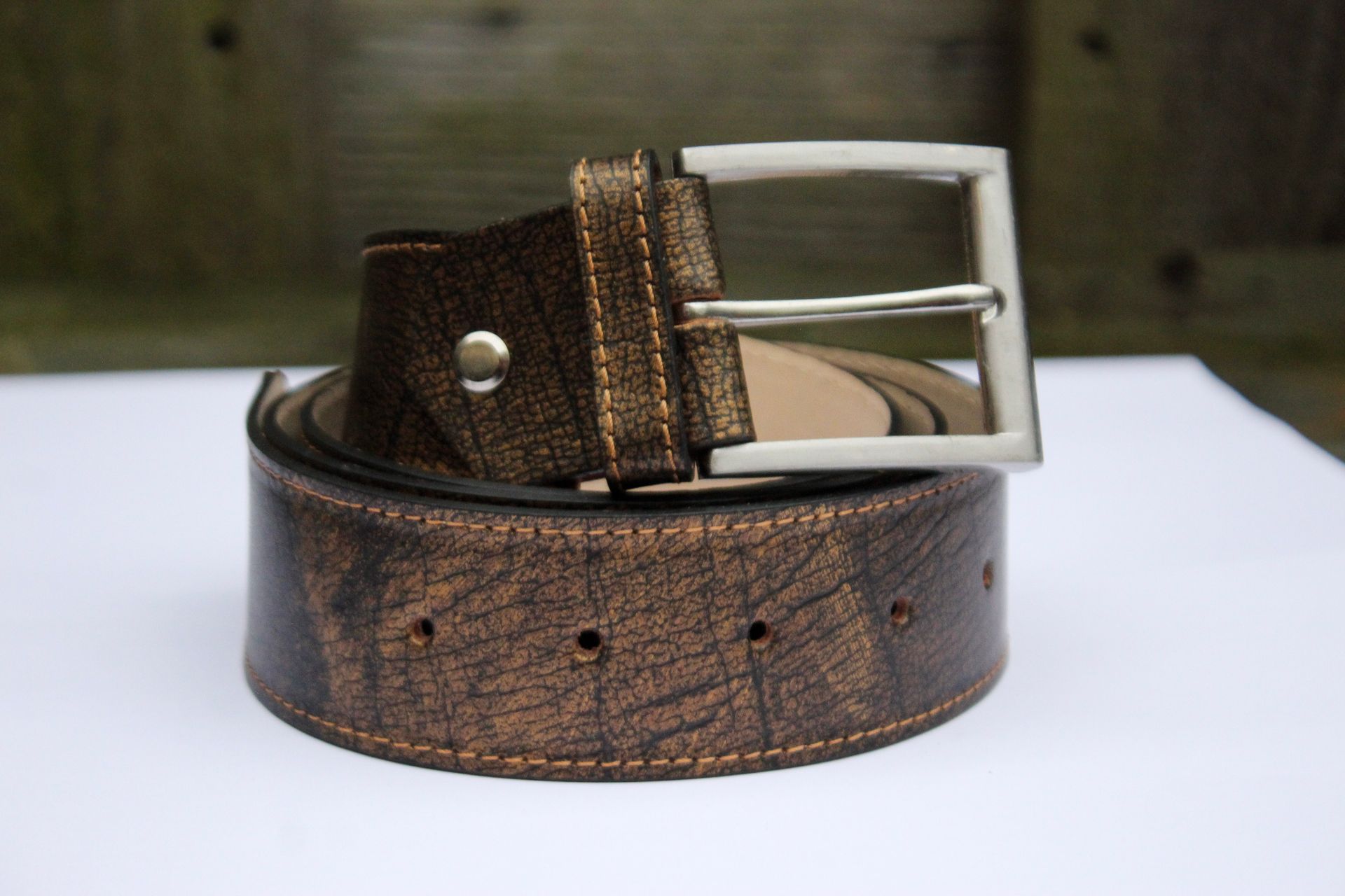 Bruine leren riem met een zilveren gesp, gerold op een witte ondergrond.