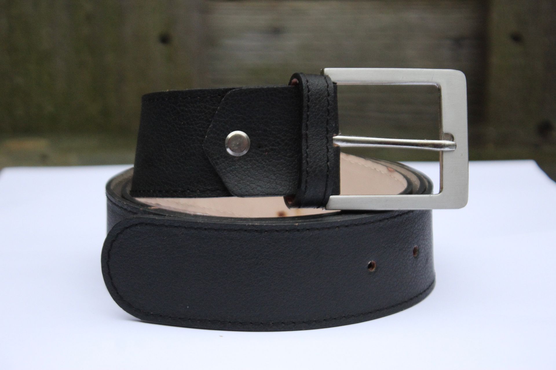 Zwarte leren riem met zilveren gesp, gerold op een witte ondergrond.