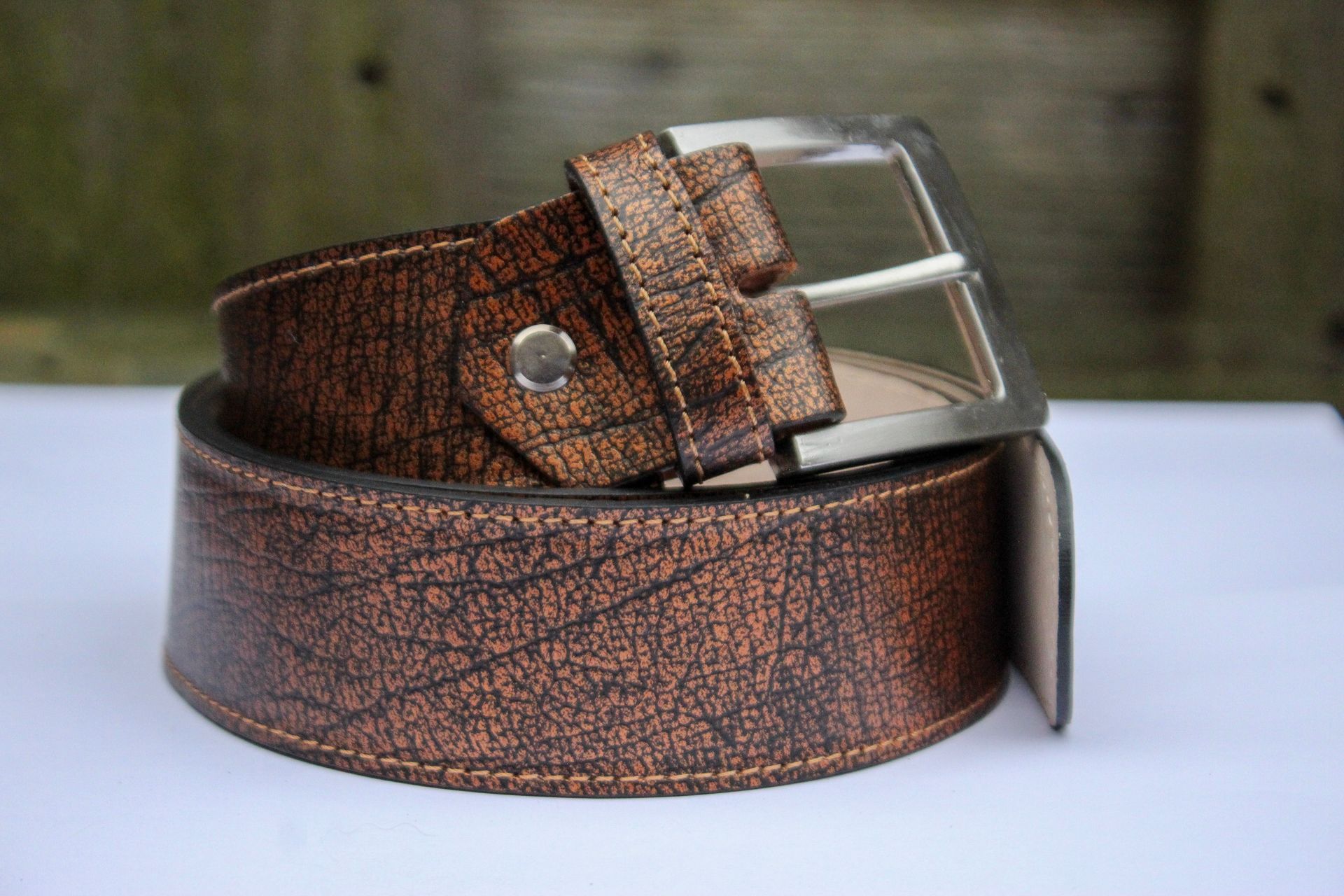 Bruine leren riem met een zilveren gesp, opgerold op een witte ondergrond.