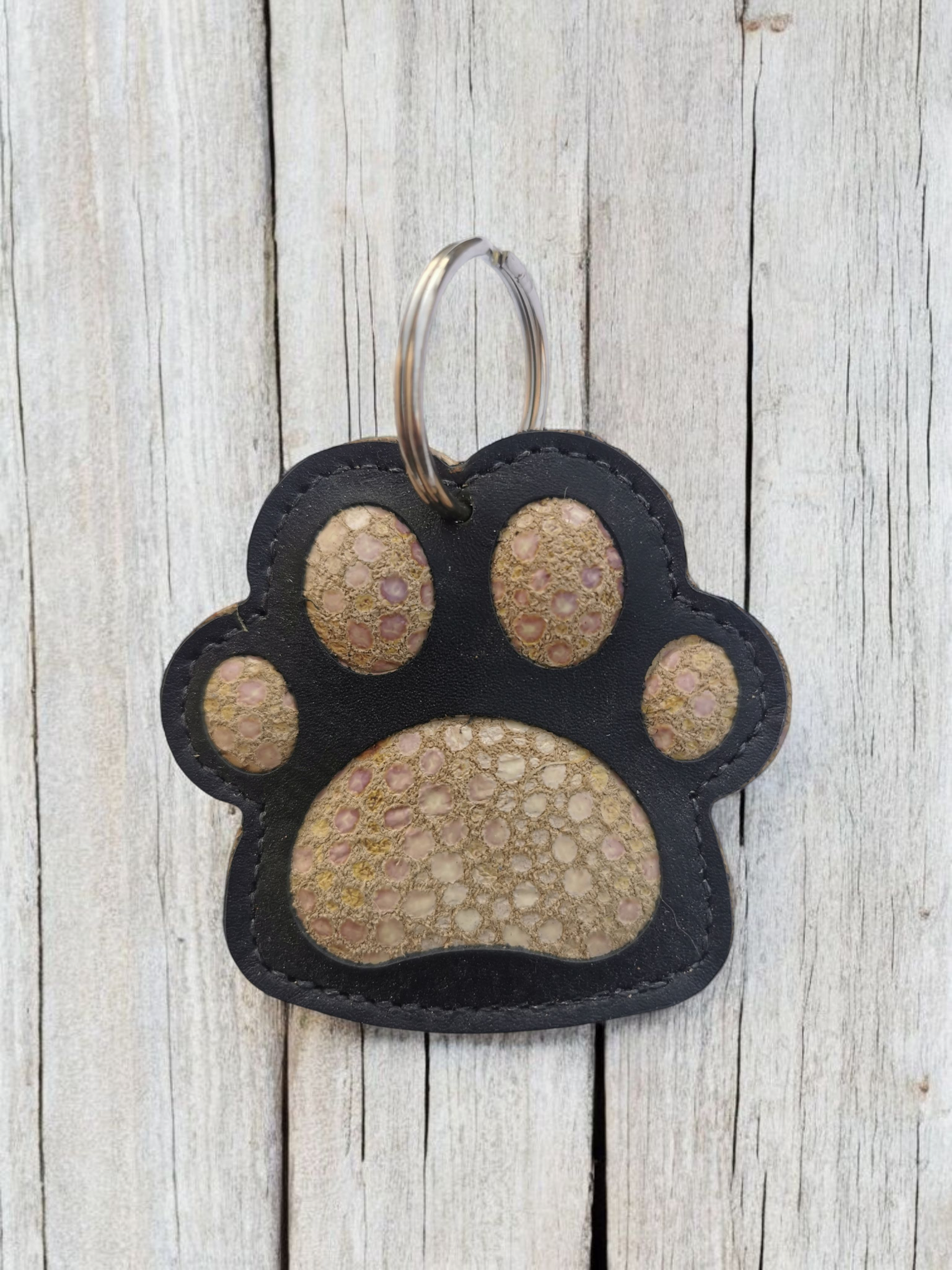 Sleutelhanger met pootafdruk, zwart en bruin met een zilveren ring, rustend op een houten ondergrond.