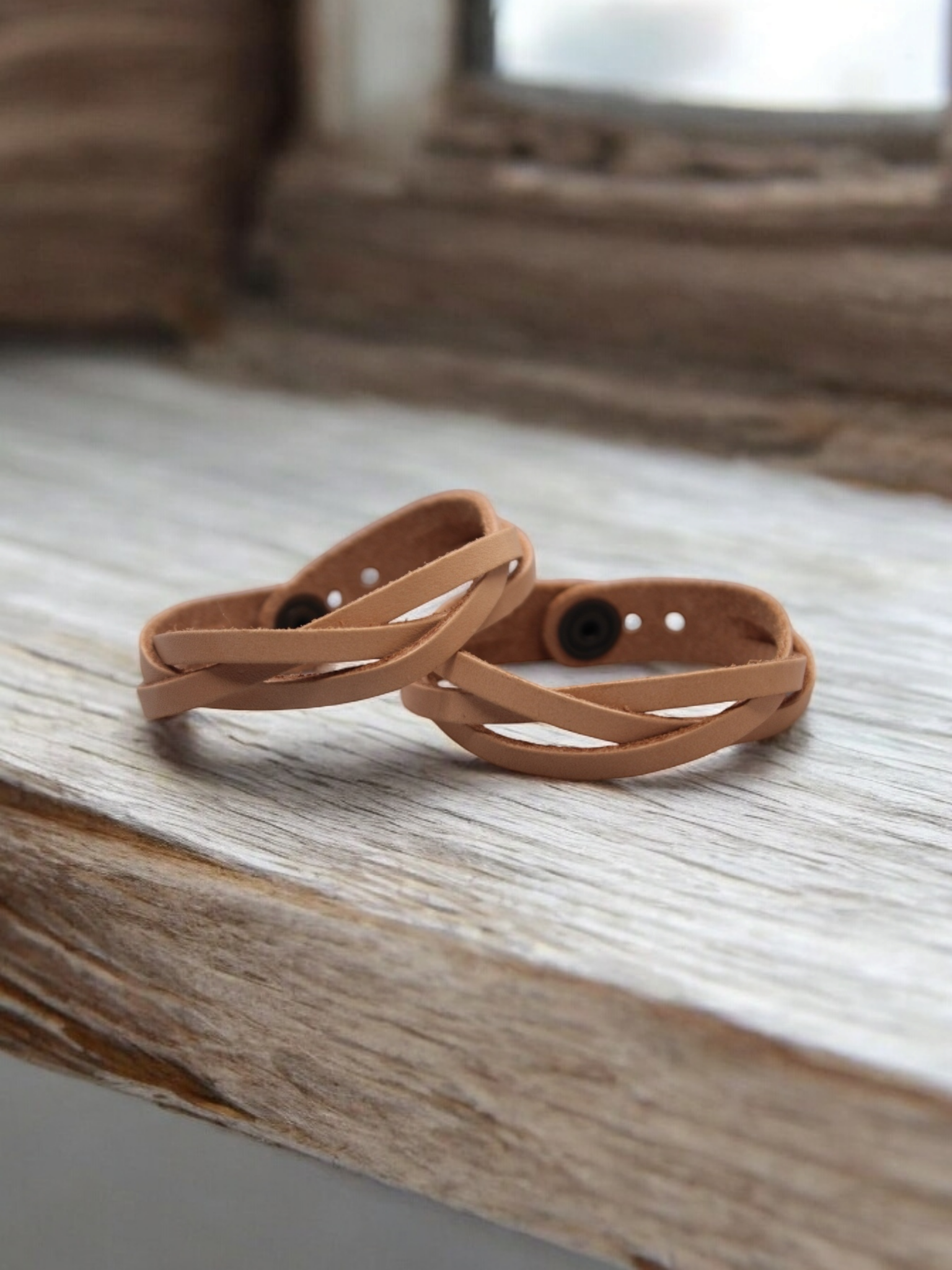 Twee lichtbruine leren armbanden gevlochten op een houten ondergrond.