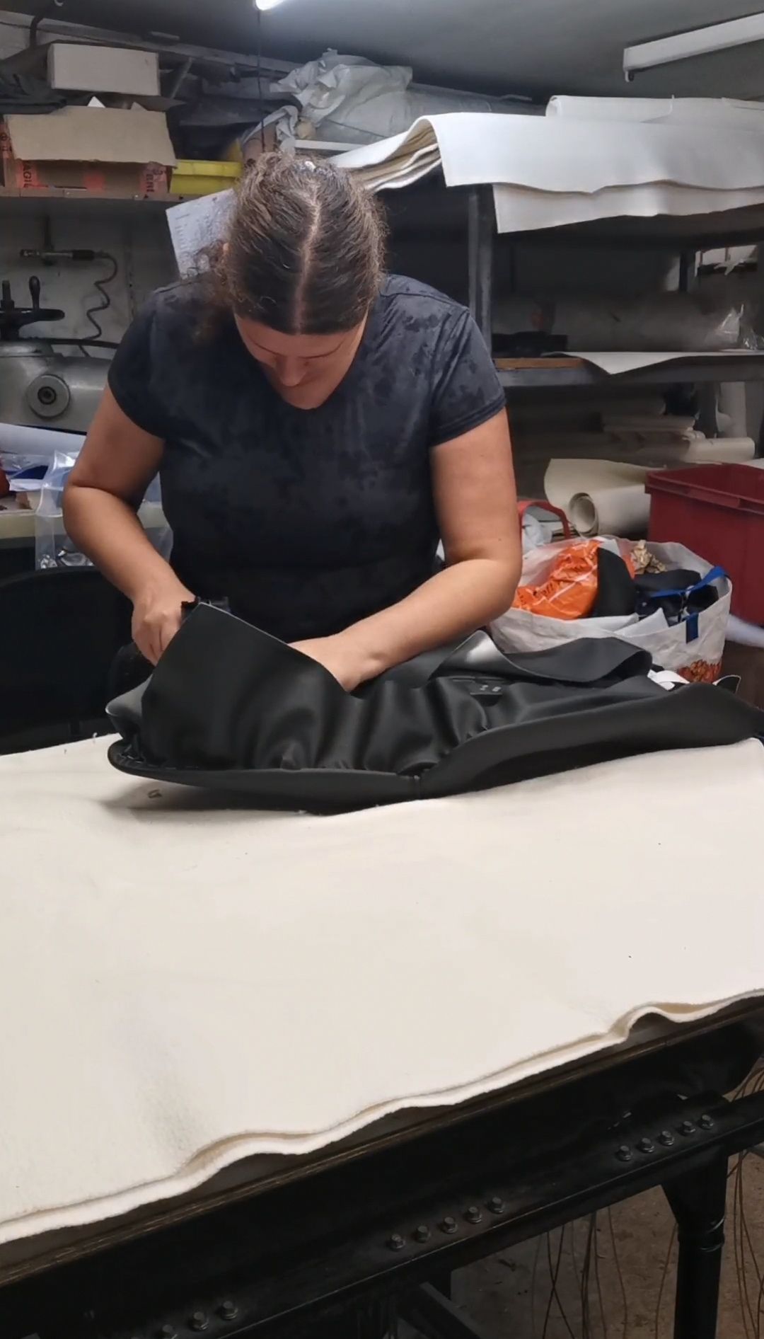 Een vrouw knipt stof in een atelier en werkt aan een zwarte tas met witte stof ernaast.
