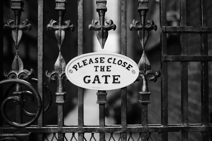 Black and white photo of an ornate wrought iron gate with a sign that says 