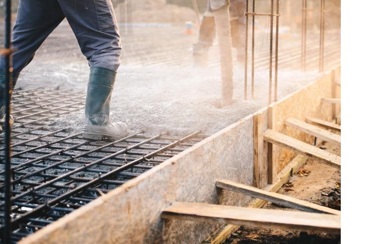 Construction worker pouring concrete onto rebar and wooden forms.