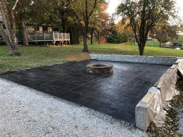 A newly constructed outdoor fire pit area with a concrete retaining wall, gravel and a fire ring.
