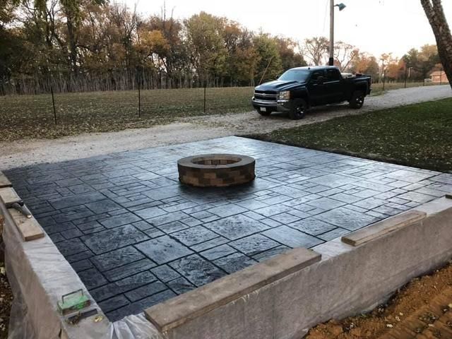 Stamped concrete patio with a fire pit, bordered by concrete blocks, and a truck parked nearby.