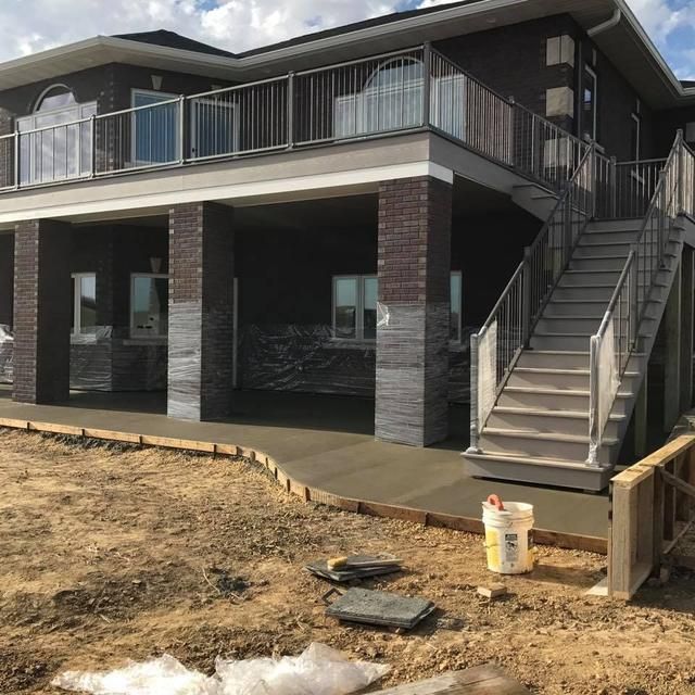 Two-story house with a concrete patio under a balcony. Staircase, brick columns, and a dirt yard.