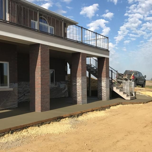Two-story house with brick pillars, a concrete patio, and a stairway under construction.
