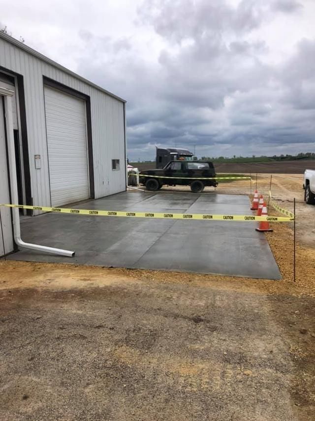 A new concrete pad outside a building, roped off with caution tape, truck parked nearby.