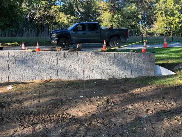 Pickup truck parked behind a gray retaining wall, orange cones, and caution tape on a road.