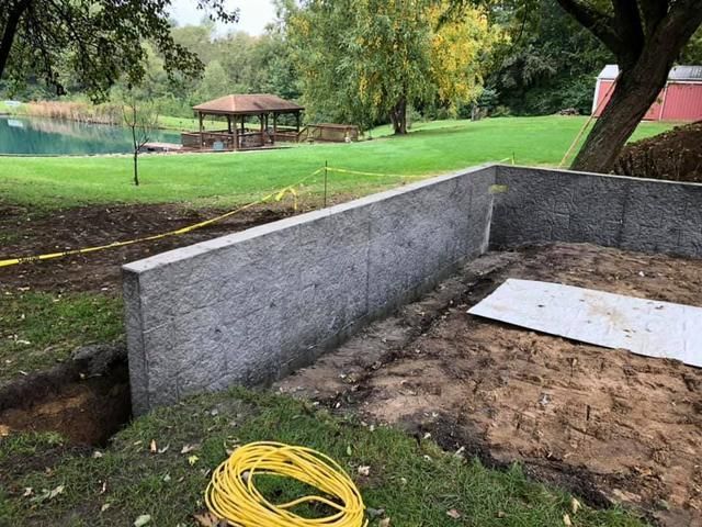 Concrete retaining wall under construction in a grassy yard, with a gazebo and water in the background.