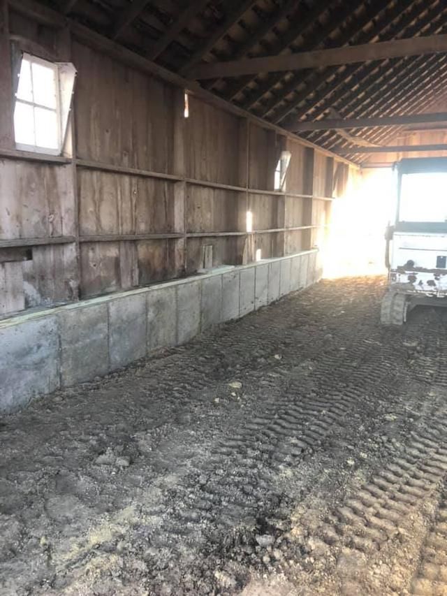 Inside a weathered barn; concrete wall along a dirt floor, light streams in.