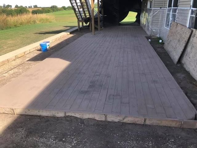 Concrete patio with brick pattern, low stone wall, and part of a house.