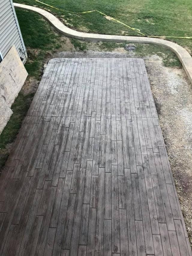 Stamped concrete patio with a weathered wood pattern. Surrounding area is gravel, grass, and a concrete walkway.