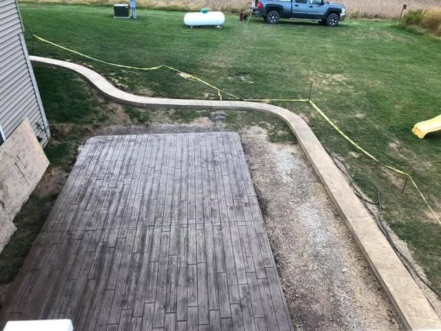 Concrete patio and walkway with a brick pattern, next to a grassy area with a truck, propane tank, and person.