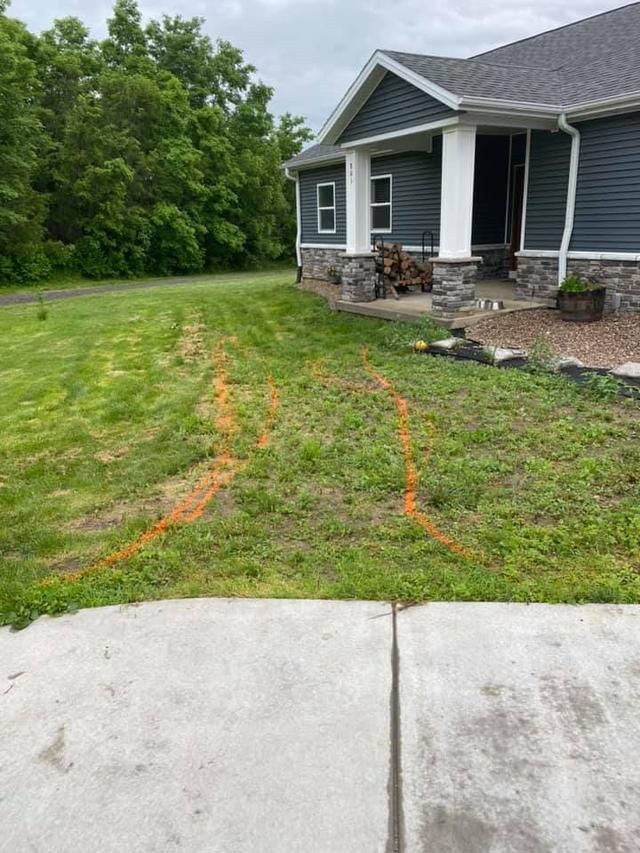 Grass yard with orange spray paint markings near a house. Driveway is in foreground.