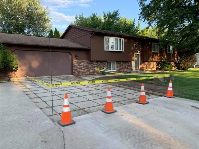 Driveway under construction, outlined with caution tape and traffic cones in front of a brown house.