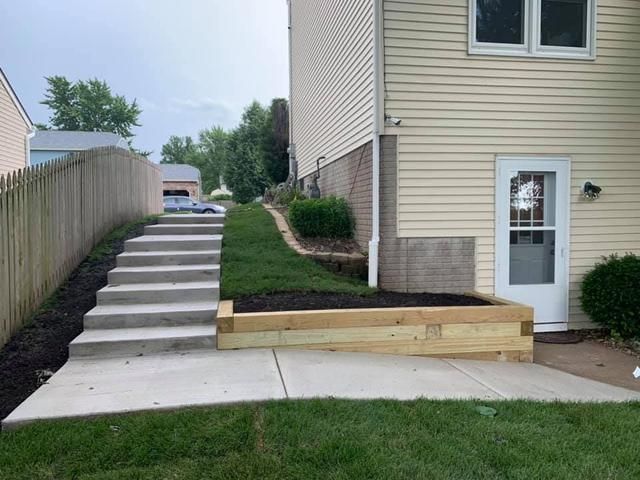 Concrete stairs and retaining wall lead up a sloping yard beside a house with a door.