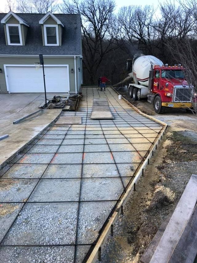 Construction of a driveway: Concrete truck pouring cement over rebar grid. House in the background.