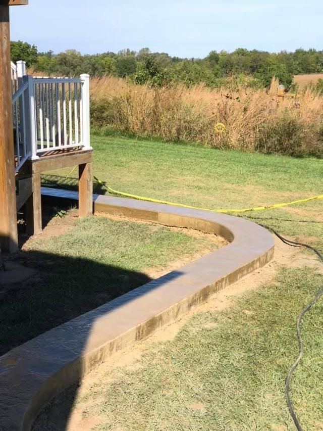 Curving concrete walkway next to a deck, set in a grassy yard.