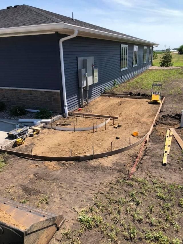 Construction site: foundation for a curved patio near a blue-sided house.