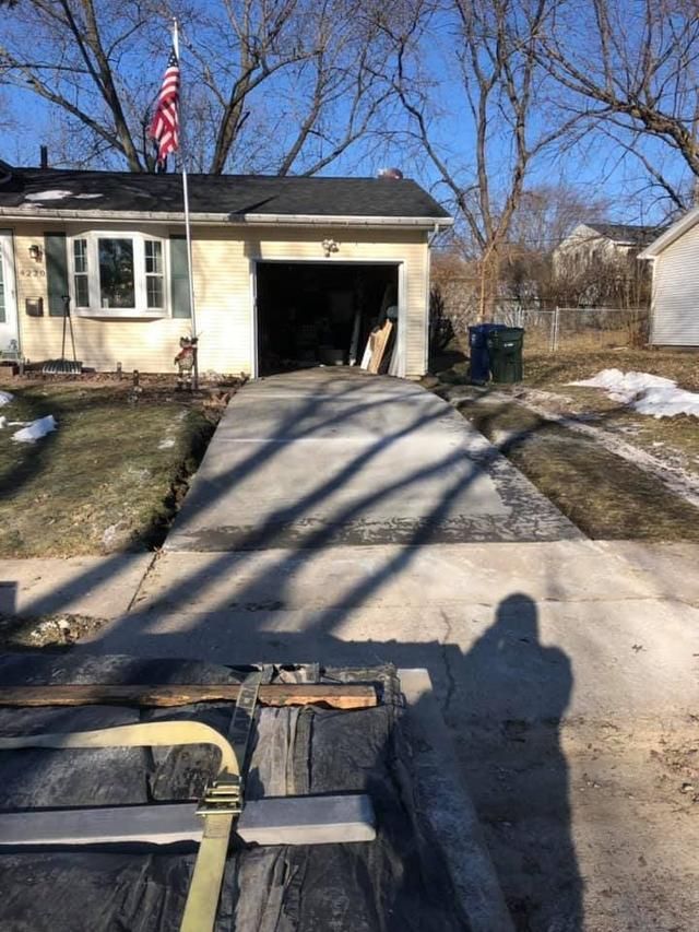 Driveway leading to a garage. An American flag flies. A person's shadow is cast on a partially removed section.