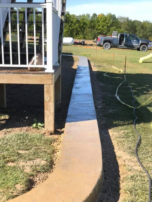 Concrete pathway alongside a deck in a backyard, partially wet.