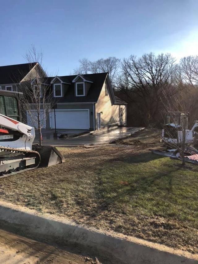 Construction site: Bobcat tractor, garage, grass, driveway under construction.