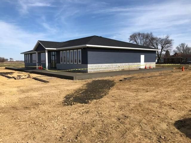 Blue building with a dark roof and a concrete sidewalk, located in a dirt lot.