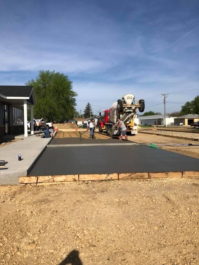 Construction crew pouring concrete for a sidewalk and driveway. Cement truck and house visible.