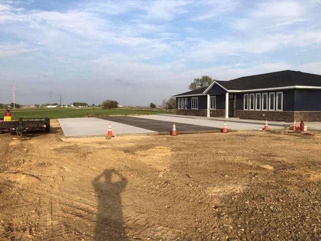 Construction site with asphalt and concrete path leading to a blue building; orange cones present.