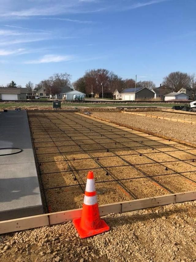 Construction site: concrete forms, rebar grid, orange traffic cone, and a freshly poured concrete slab.