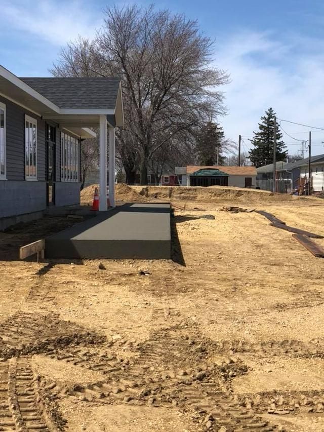 Construction site with a new house; gray porch and concrete pathway. Earth movers tracks in dirt.