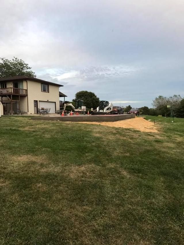 A two-story house with a concrete patio under construction, in a grassy backyard, cloudy sky.