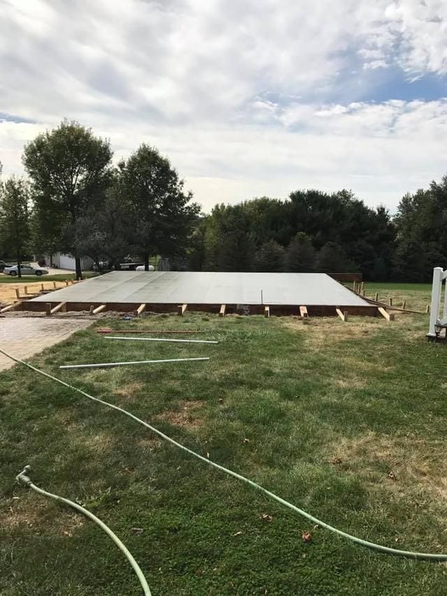 Newly poured concrete slab within wooden framing, in a grassy yard, under a cloudy sky.