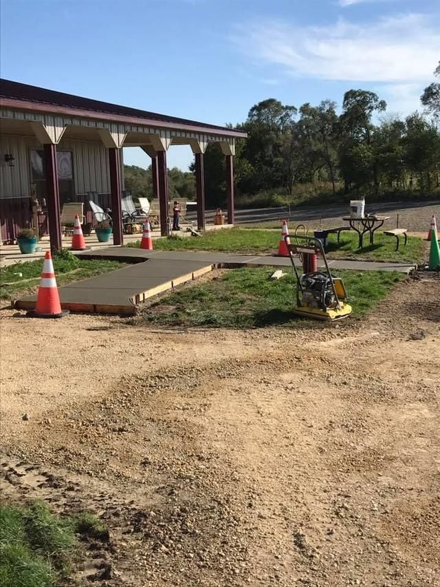 Concrete slab being poured near a building with a porch; construction cones and compacting machine.