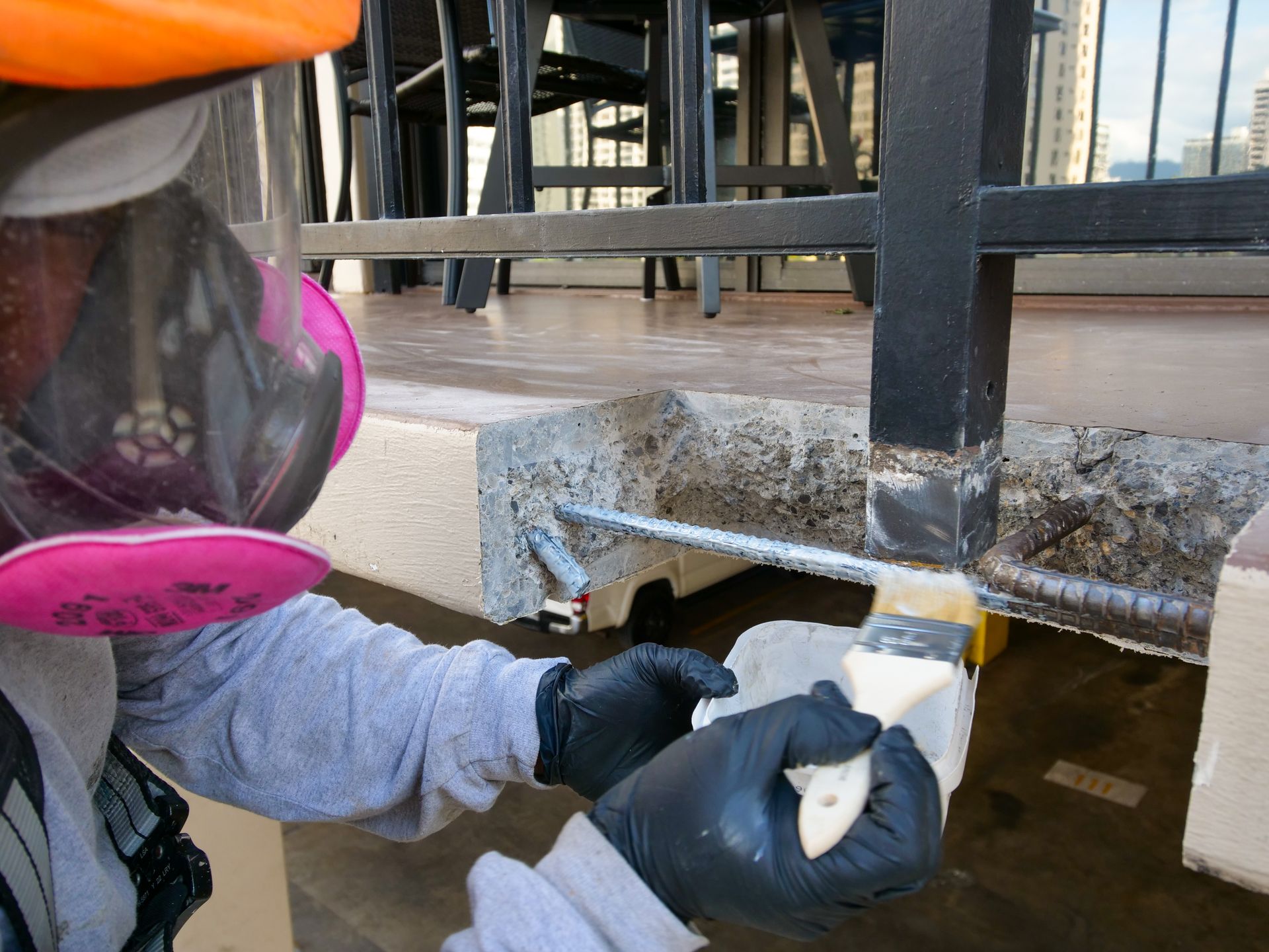 A person wearing a beekeeper 's mask and gloves is working on a balcony.