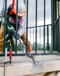 A man wearing a hard hat is working on a balcony.