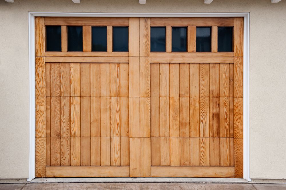 Wooden garage door with windows, framed in white, set against a light-colored wall.