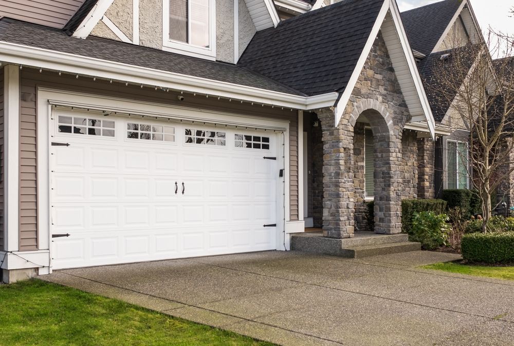 A large white garage door is parked in front of a large house.